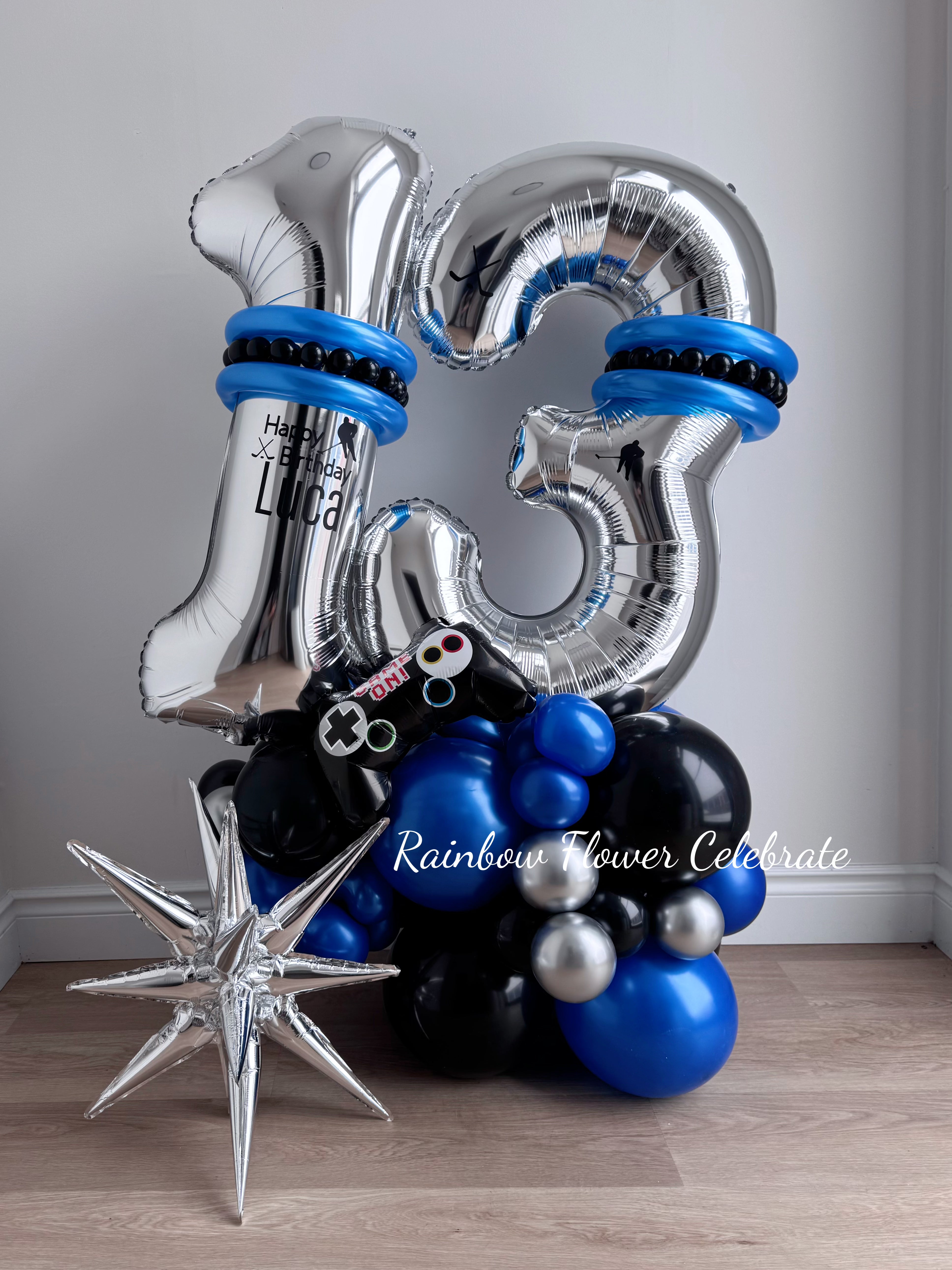 Silver '13' balloon with blue and black accents, surrounded by other balloons on a wooden floor.
