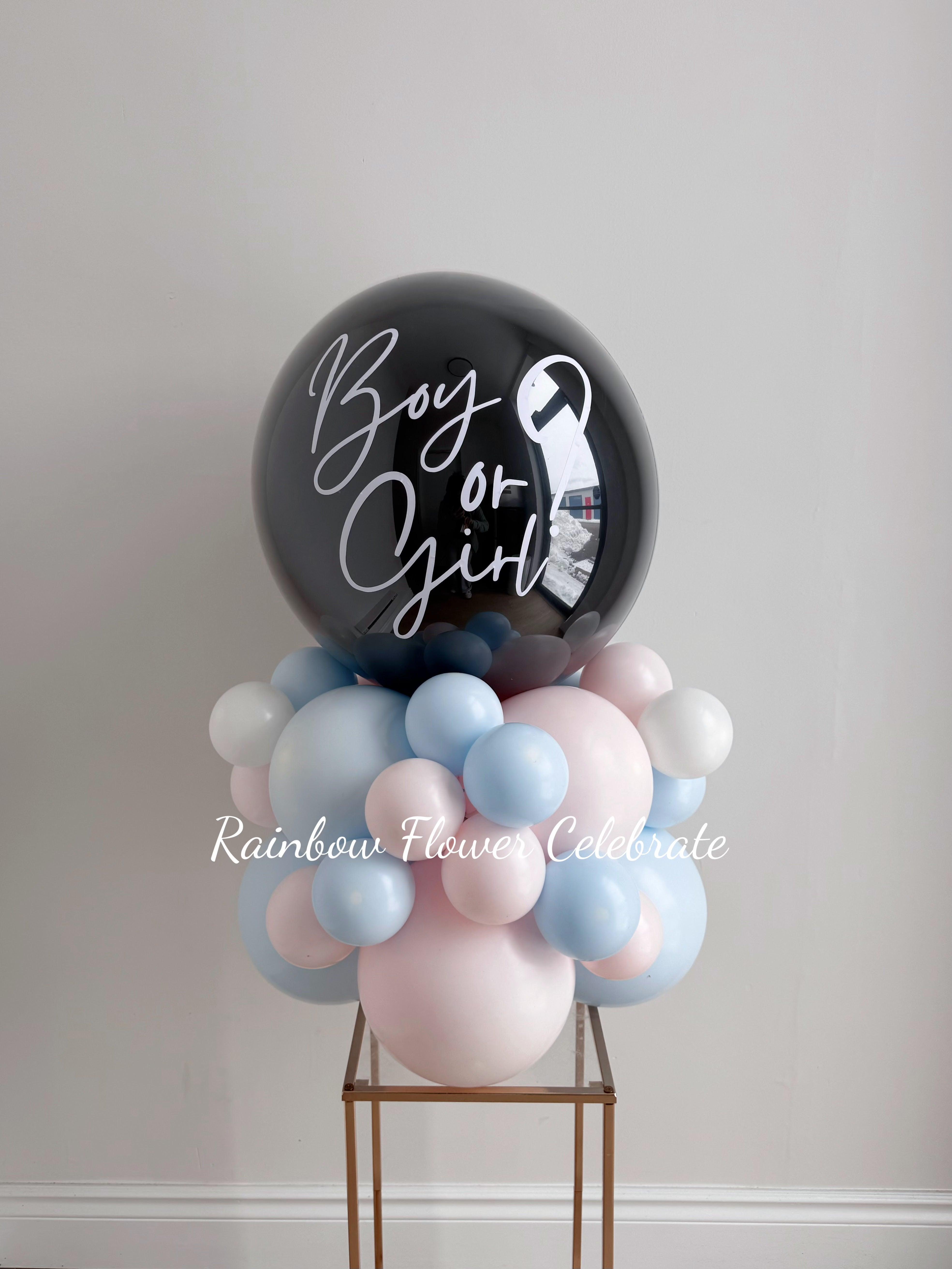 Black Gender reveal balloon on table on a pink and blue balloon base, with boy or girl? message on a black balloon
