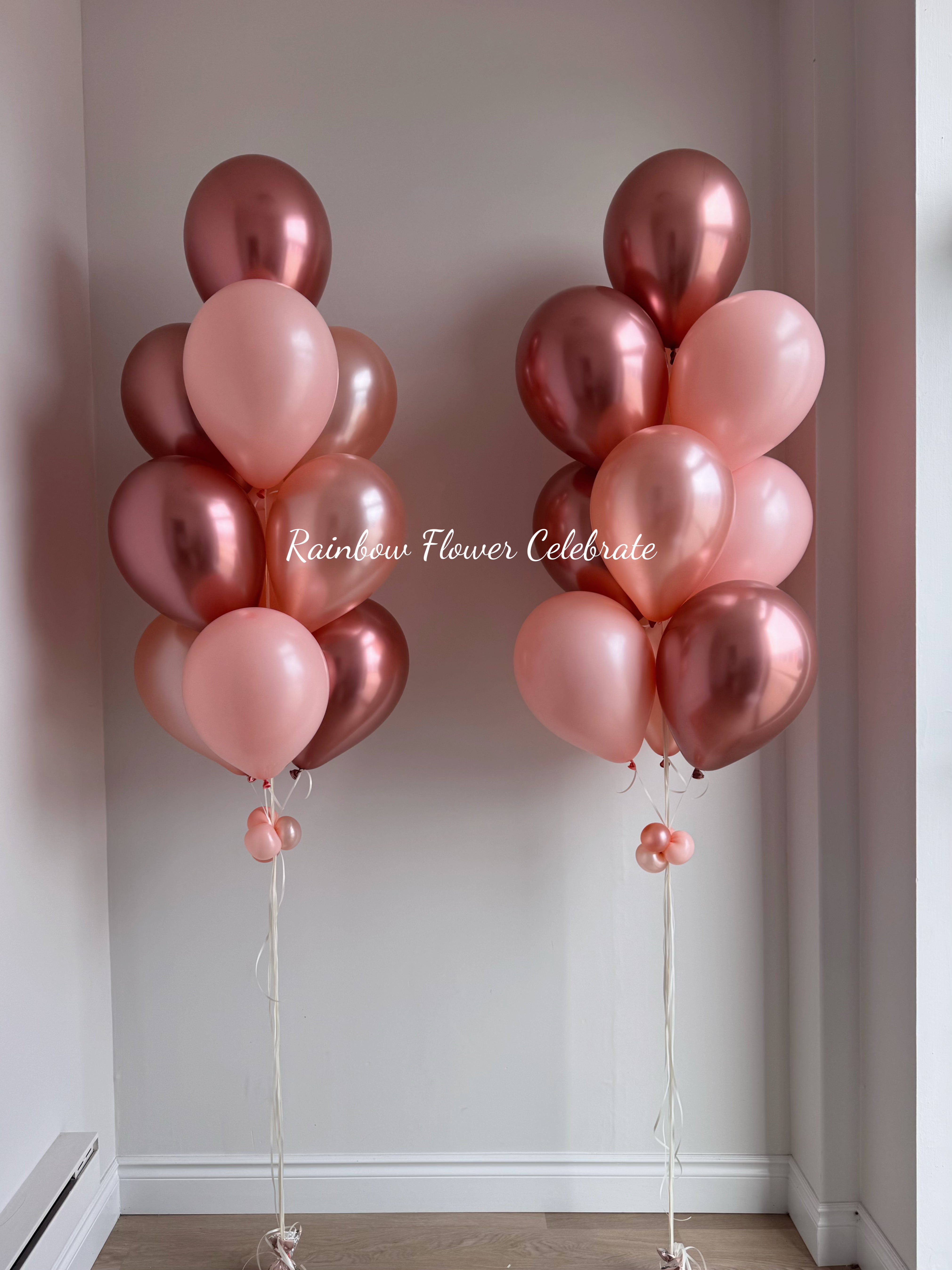 Two bunches of pink and rose gold helium balloons against a plain wall.
