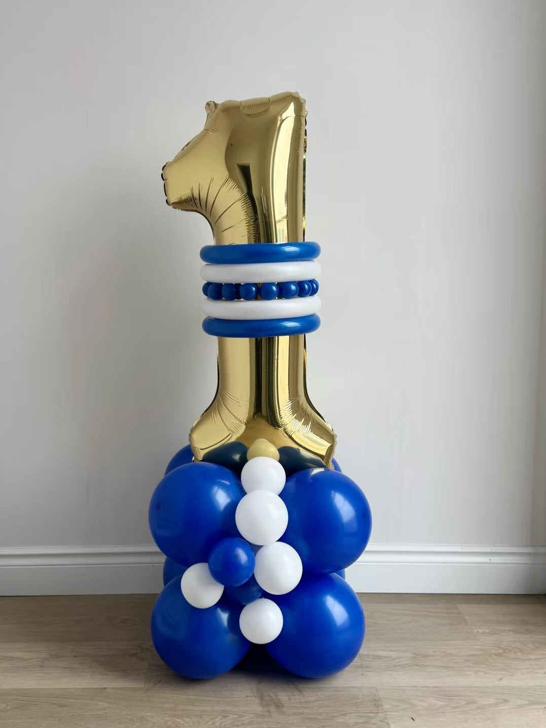 Gold number 1 balloon with blue and white balloons against a plain wall.