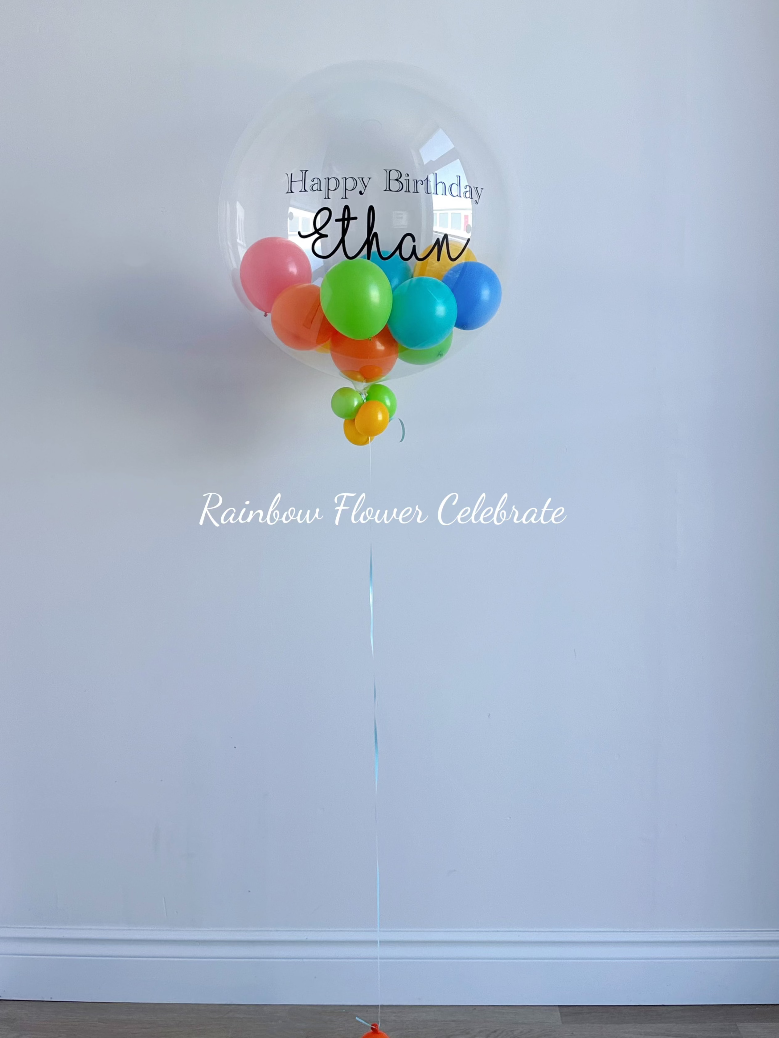 Clear balloon with colorful balloons inside against a white wall, featuring 'Happy Birthday Ethan' text.
