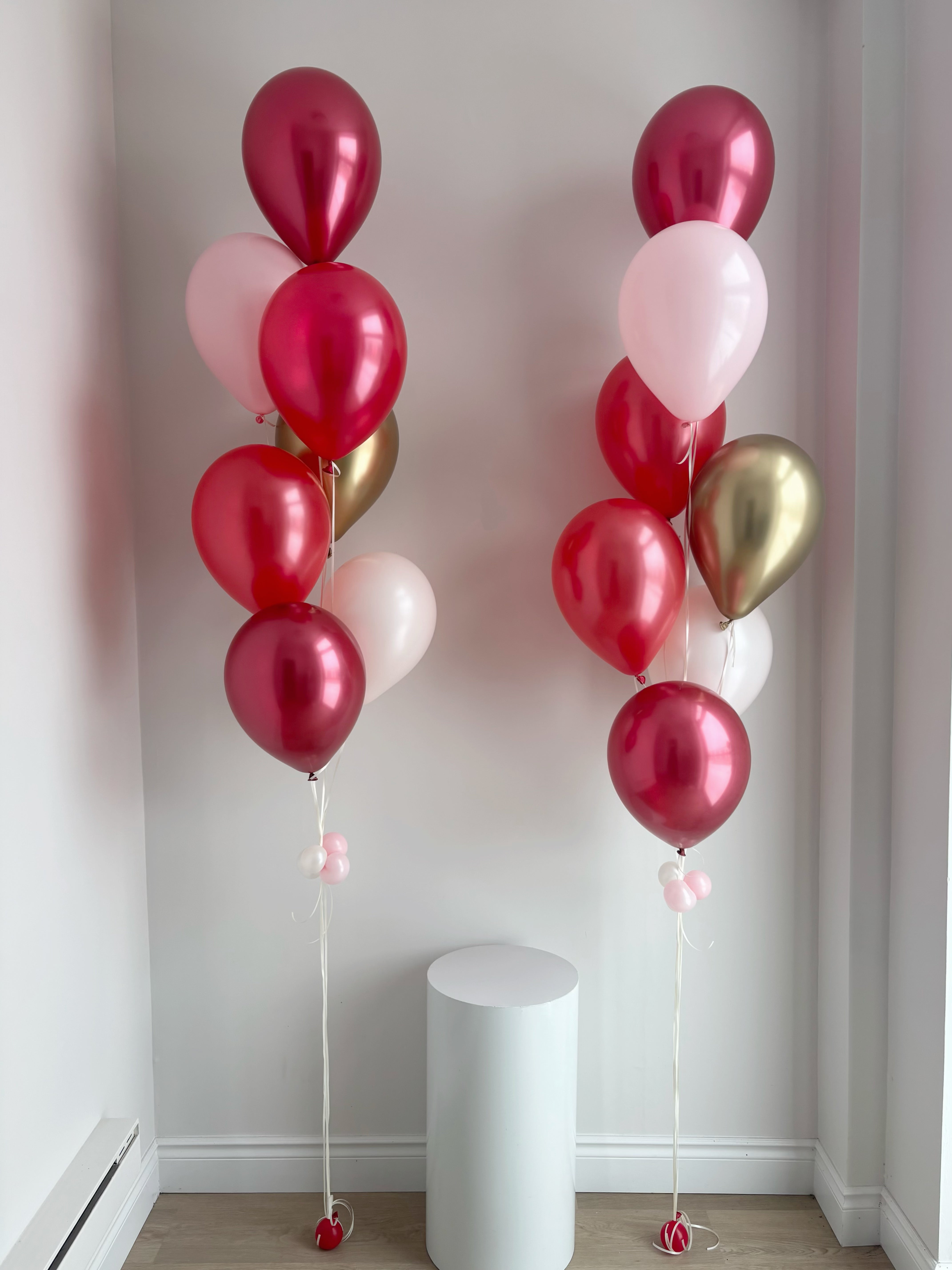 Two balloon bouquets with pink, red, gold, and white balloons in a modern room