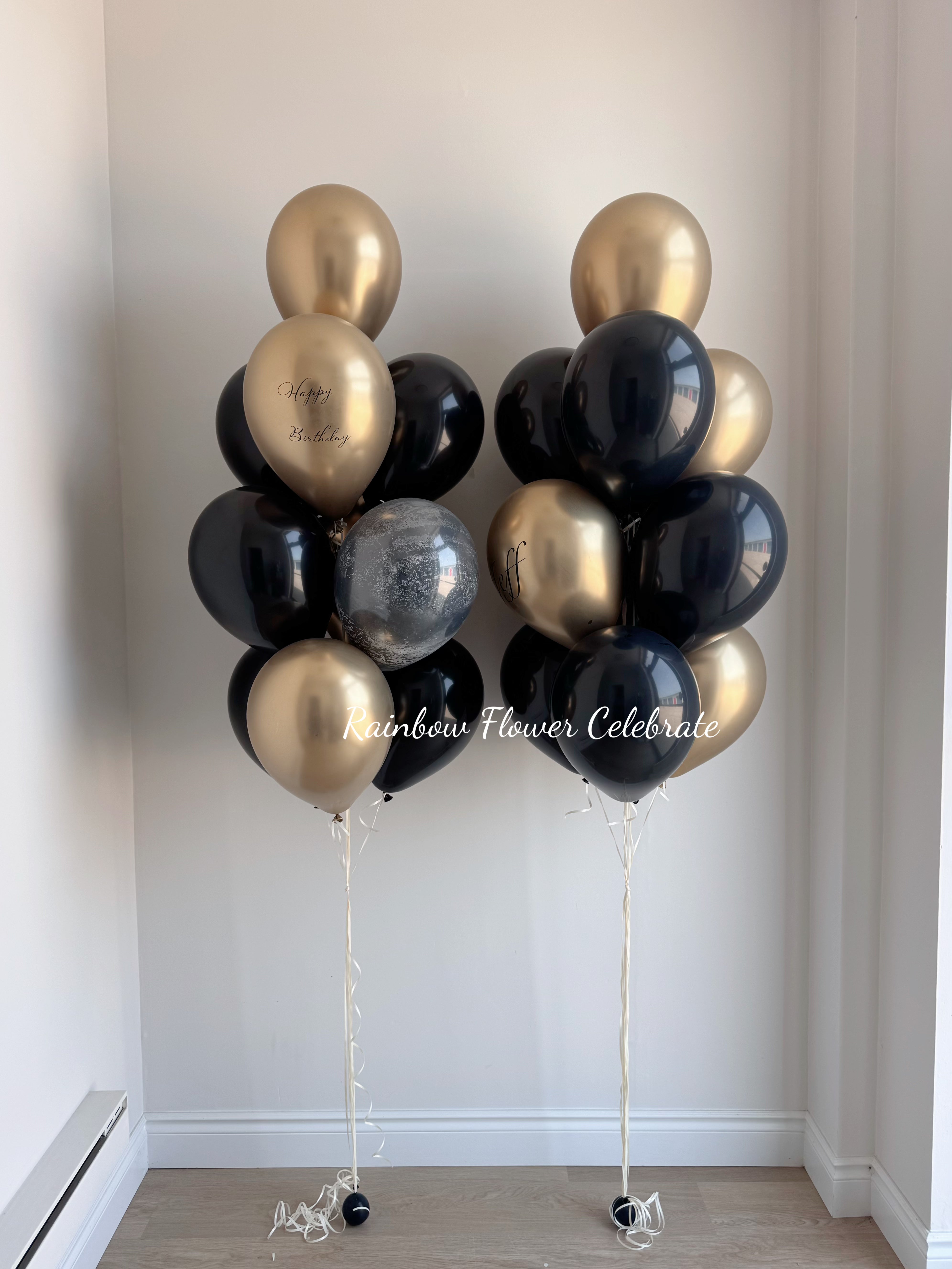 Bunch of black, gold, and silver balloons against a white wall.