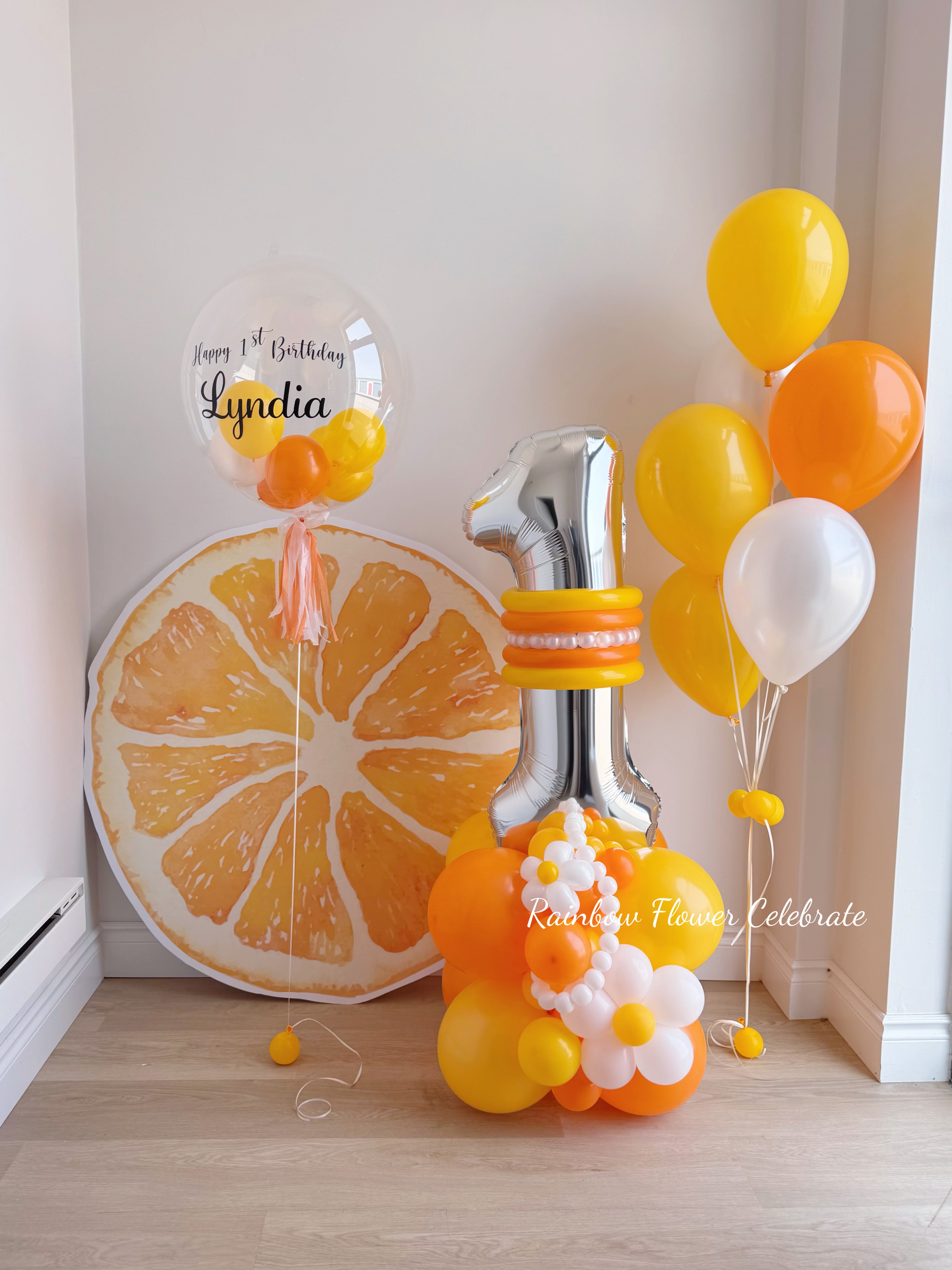 Decorative setup with balloons, number 1 balloon, and a large orange slice on a light wooden floor.