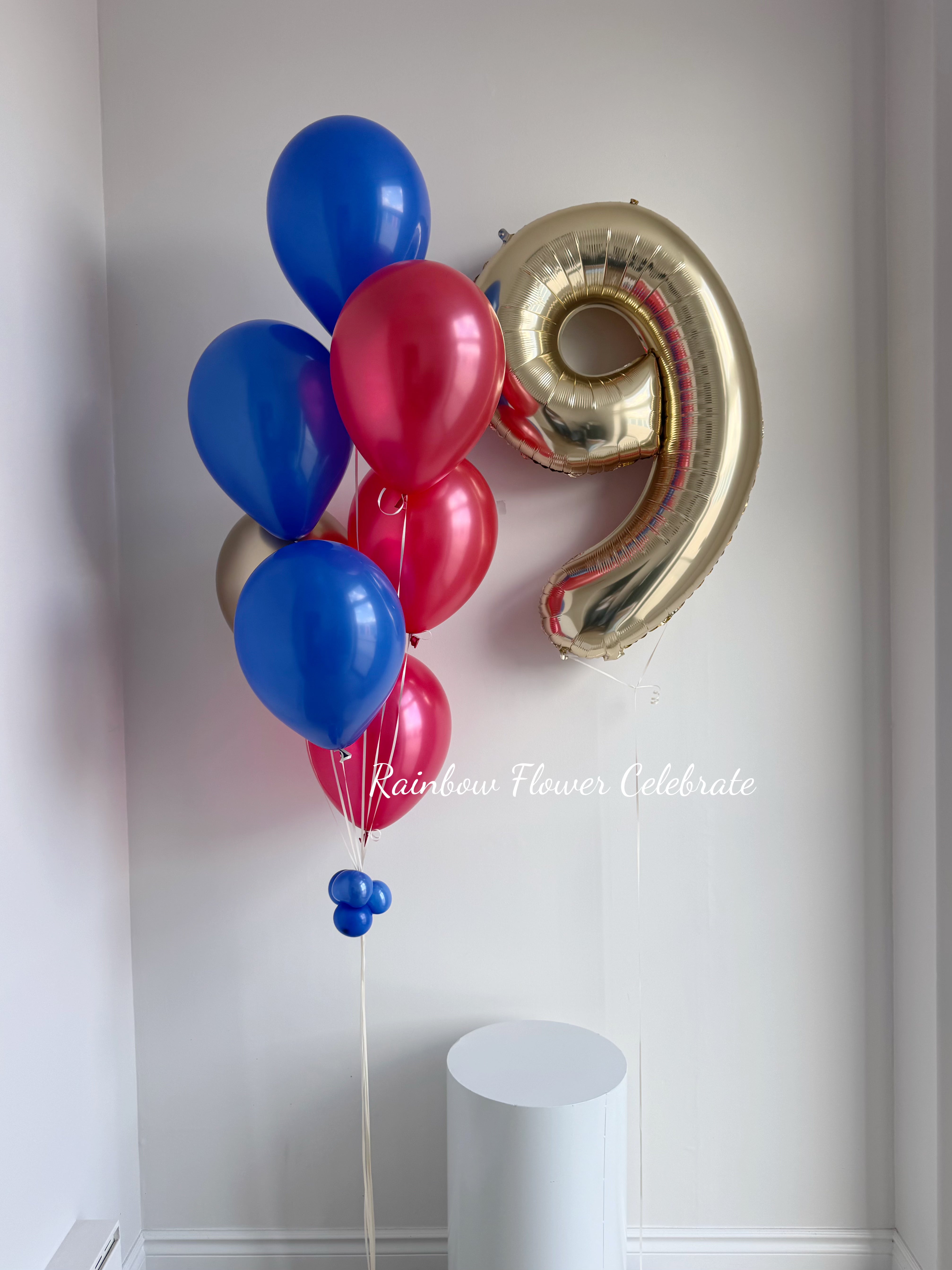 Bouquet of blue and red balloons with a gold number 9 balloon against a white wall.
