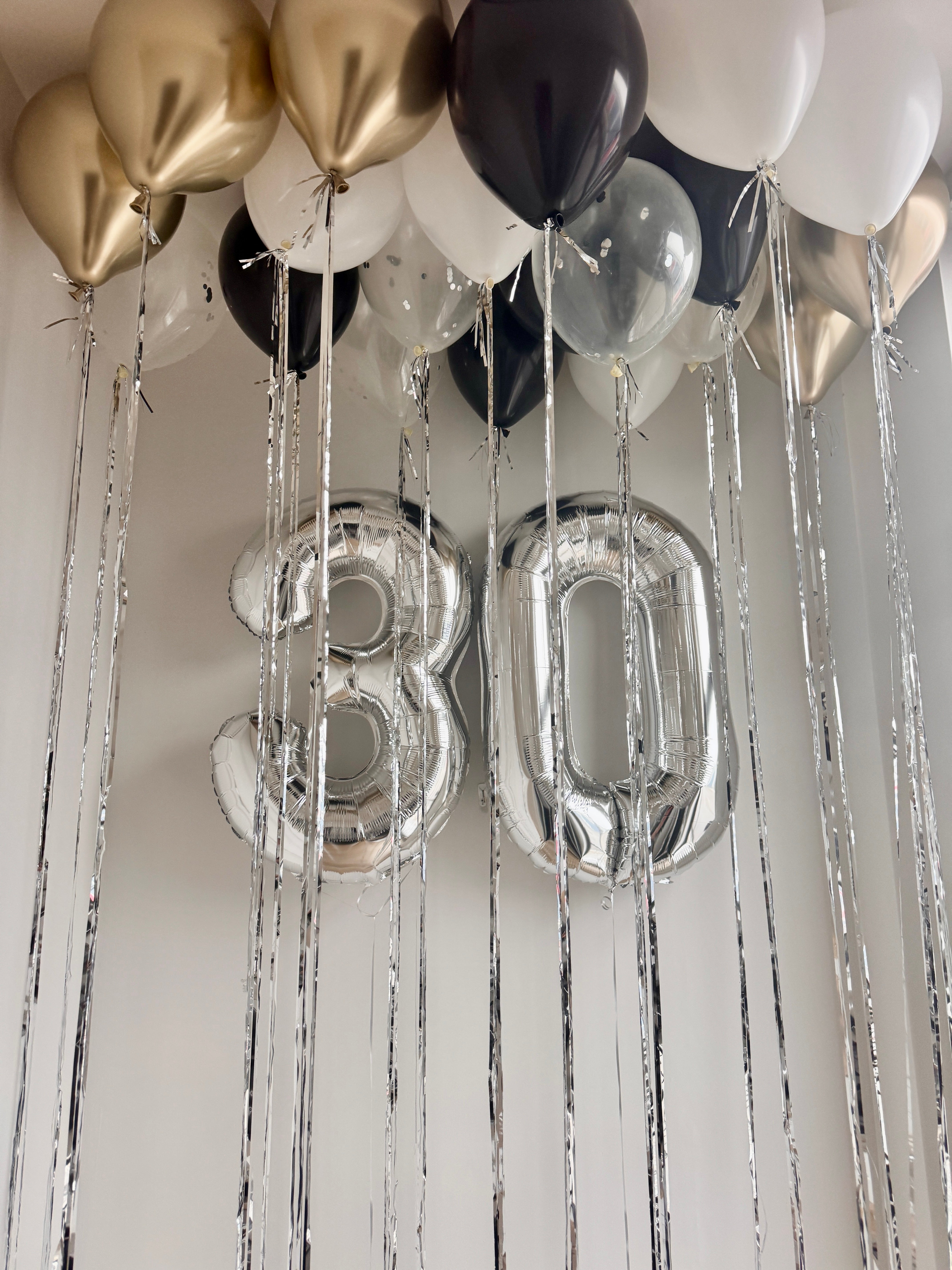 Decorative setup with balloons and '30' in silver number and gold white black balloons floating on the ceiling